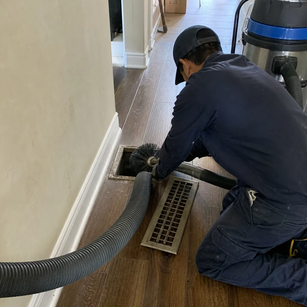 Technician using professional cleaning brush for residential air duct vent